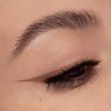 Nahaufnahme eines Auges mit cappuccinofarbenem Eyeliner. Der präzise Wing zieht sich scharf nach außen, Wimpern sind betont.