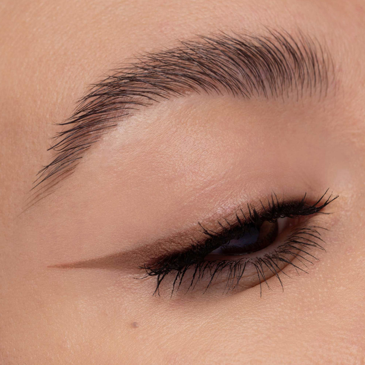 Nahaufnahme eines Auges mit cappuccinofarbenem Eyeliner. Der präzise Wing zieht sich scharf nach außen, Wimpern sind betont.