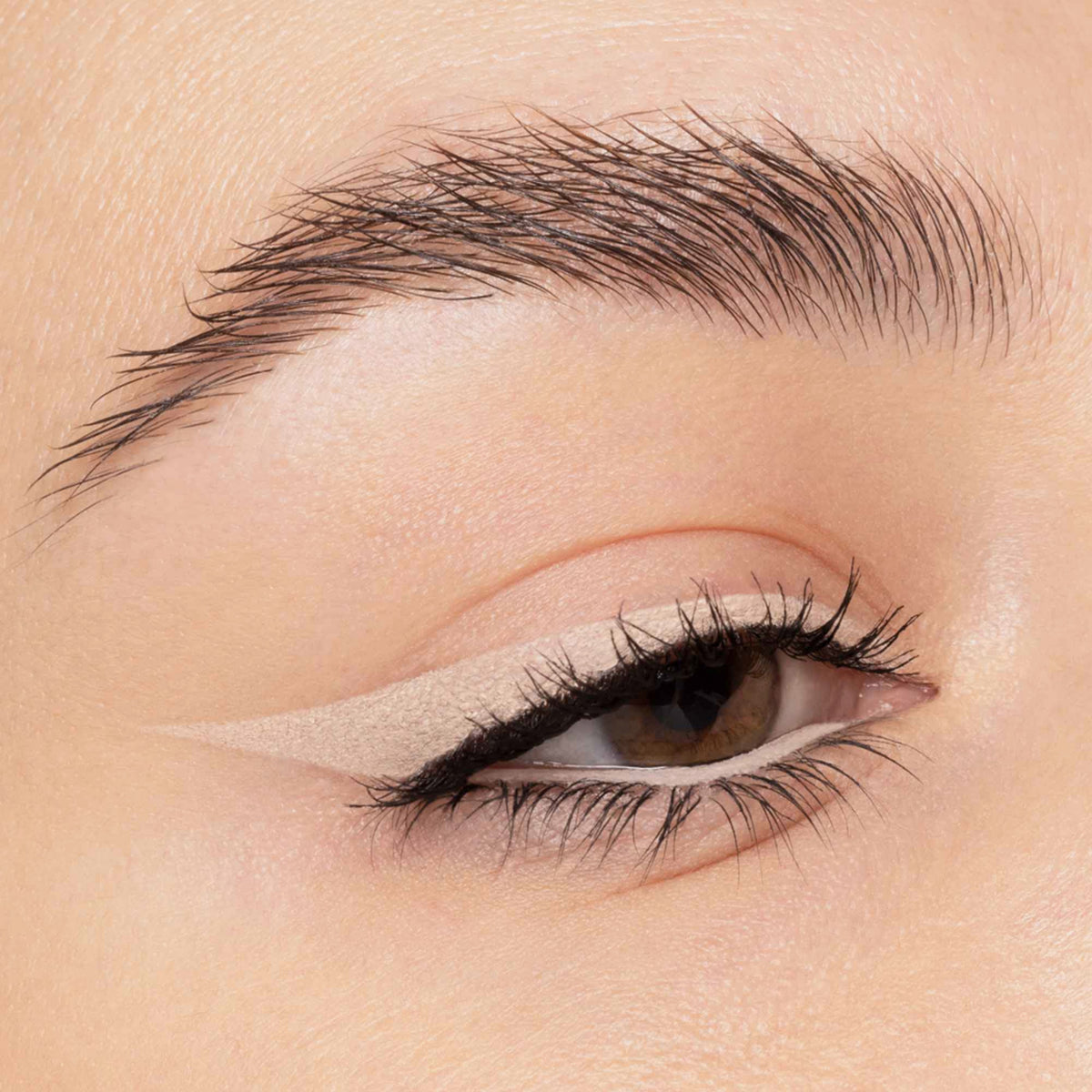 Nahaufnahme eines Auges mit beigem Eyeliner. Der präzise Wing zieht sich scharf nach außen, Wimpern sind betont.