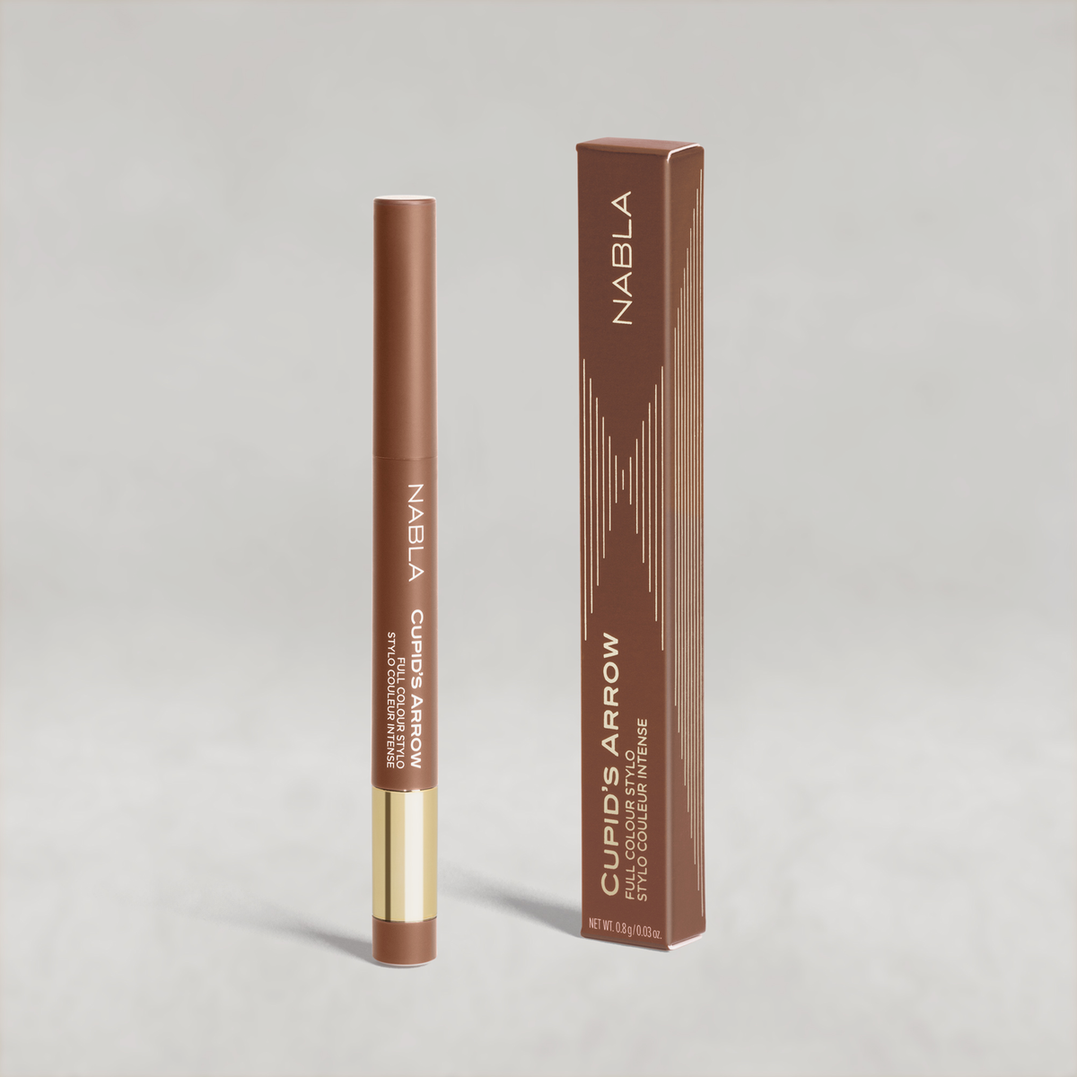 Hellbrauner Lidschatten-Stift mit goldener Kappe von NABLA neben der passenden Umverpackung mit goldenen Designelementen auf hellem Hintergrund.