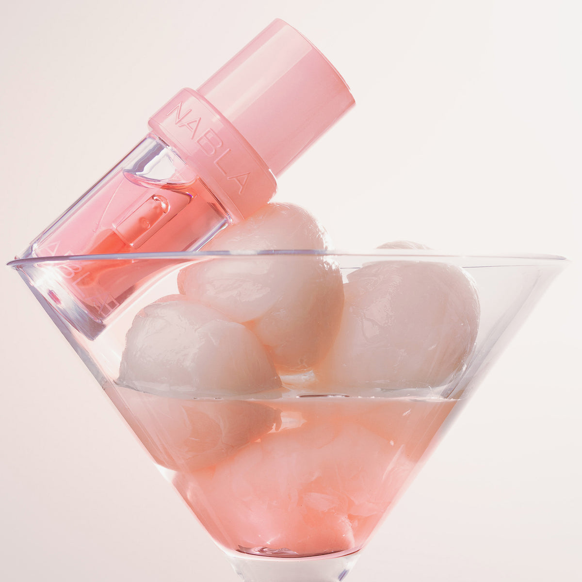 Lip Candy Oil sitzt auf Eiskugeln in einem Martini-Glas, das mit hellrosa Flüssigkeit gefüllt ist.