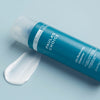 Eine blaue Flasche Skin Balancing Oil-Reducing Cleanser wird mit der Creme auf einer hellblauen Oberfläche präsentiert.