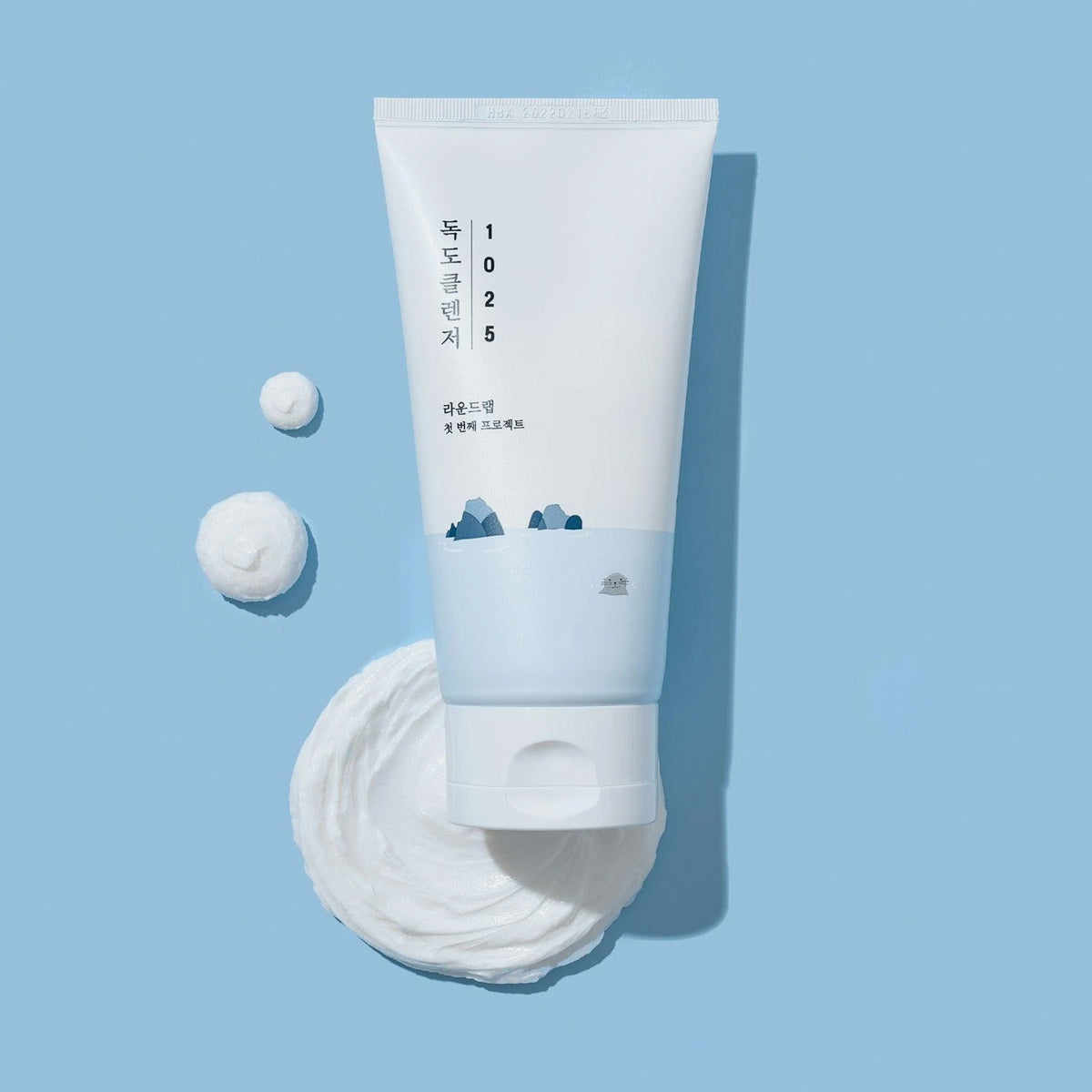 Auf einem hellblauen Hintergrund ist eine blau-weiße Tube 1025 Dokdo Cleanser mit Reinigungsschaum daneben abgebildet.