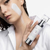 Frau mit aufgetragener Creme auf der Wange hält den Skintegra UNA Moisturizer in der Hand.