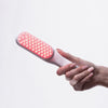 Eine Hand hält die STYLPRO Re-Growth Red Light Hair Brush, deren Borsten mit roten LED-Lichtern beleuchtet sind, vor einem weißen Hintergrund.