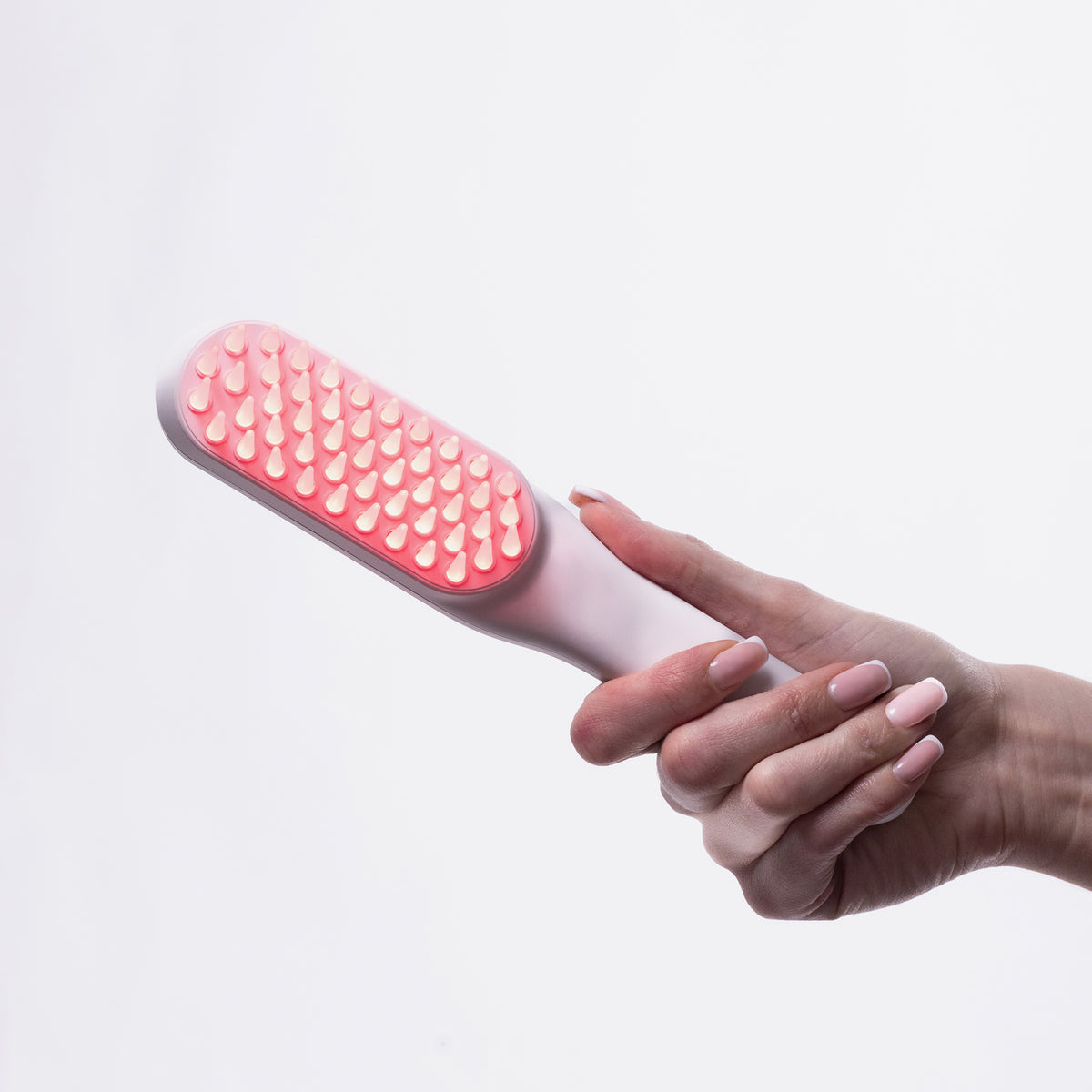Eine Hand hält die STYLPRO Re-Growth Red Light Hair Brush, deren Borsten mit roten LED-Lichtern beleuchtet sind, vor einem weißen Hintergrund.