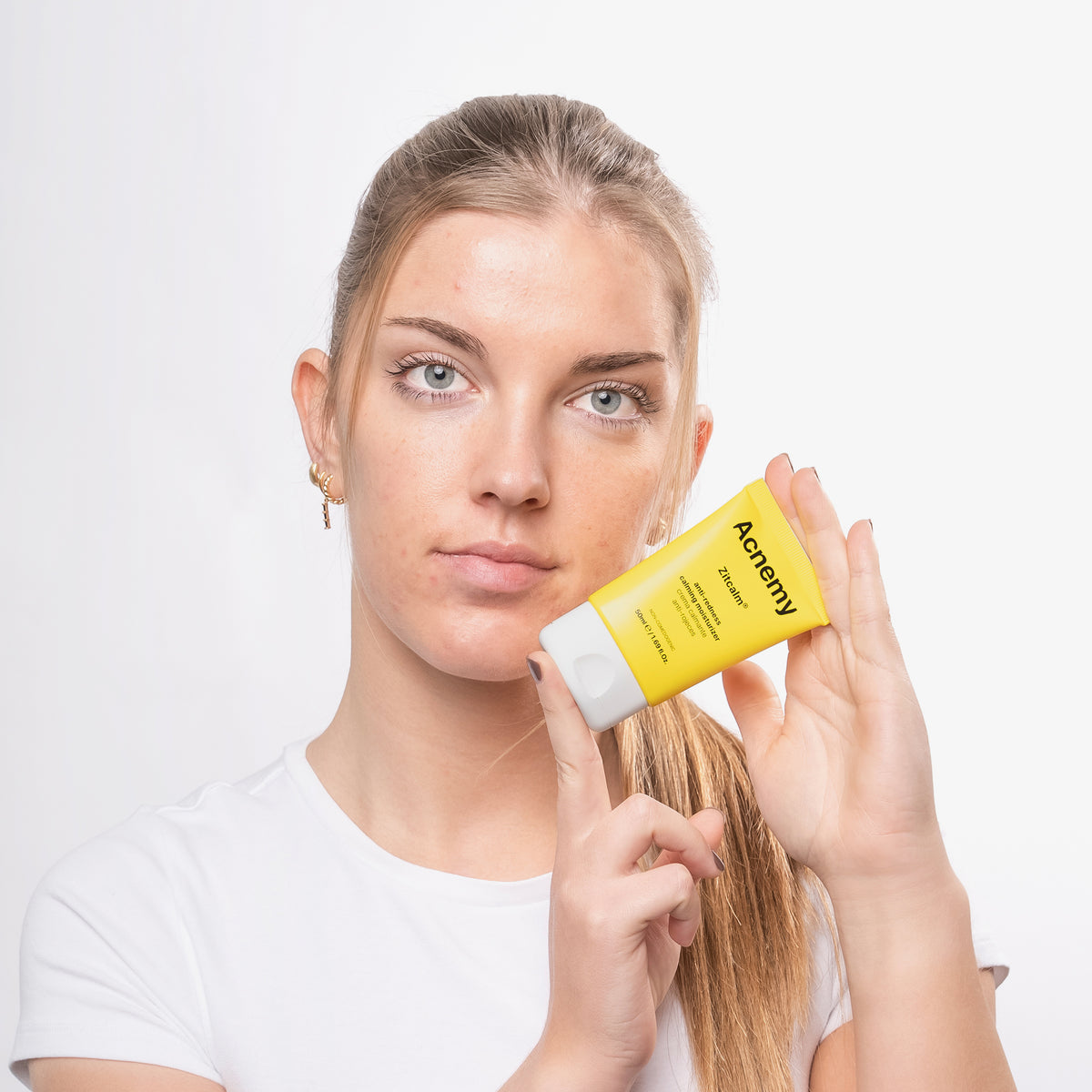 Eine Person in einem weißen Shirt hält vor einem weißen Hintergrund eine gelbe Tube Zitcalm Moisturizer.