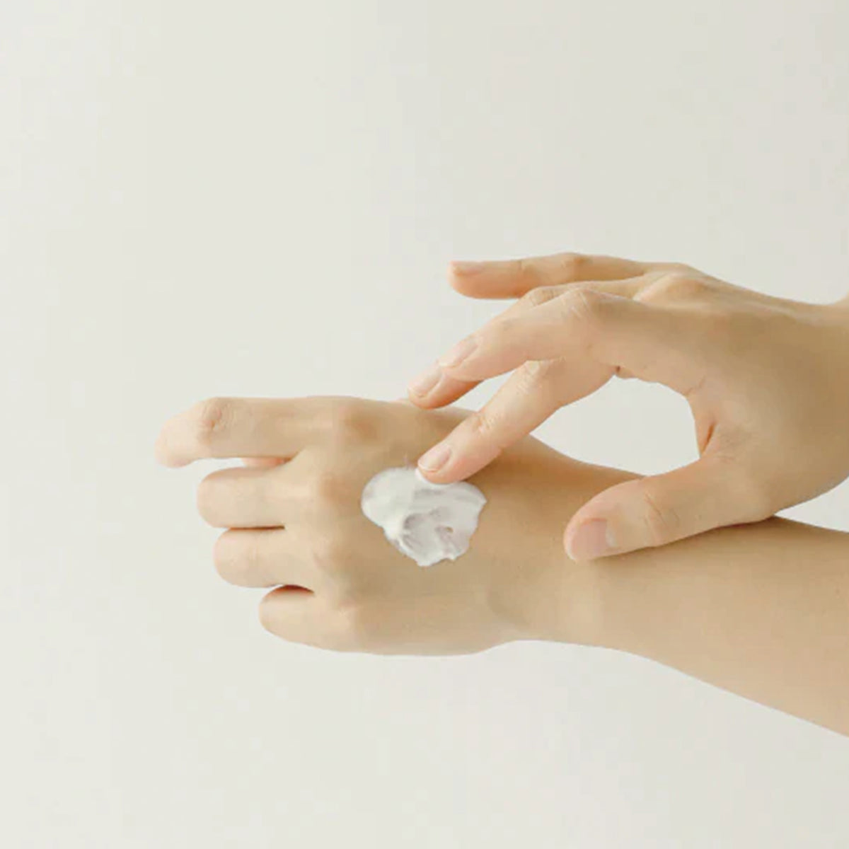 Hände, die Relief Sun: Rice + Probiotics auf den Handrücken auftragen, vor einem schlichten Hintergrund