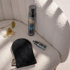 Der Application Mitt, die Self Tan Drops, das Self Tanning Foam Dark und eine Sonnenbrille liegen auf einem weißen Sessel
