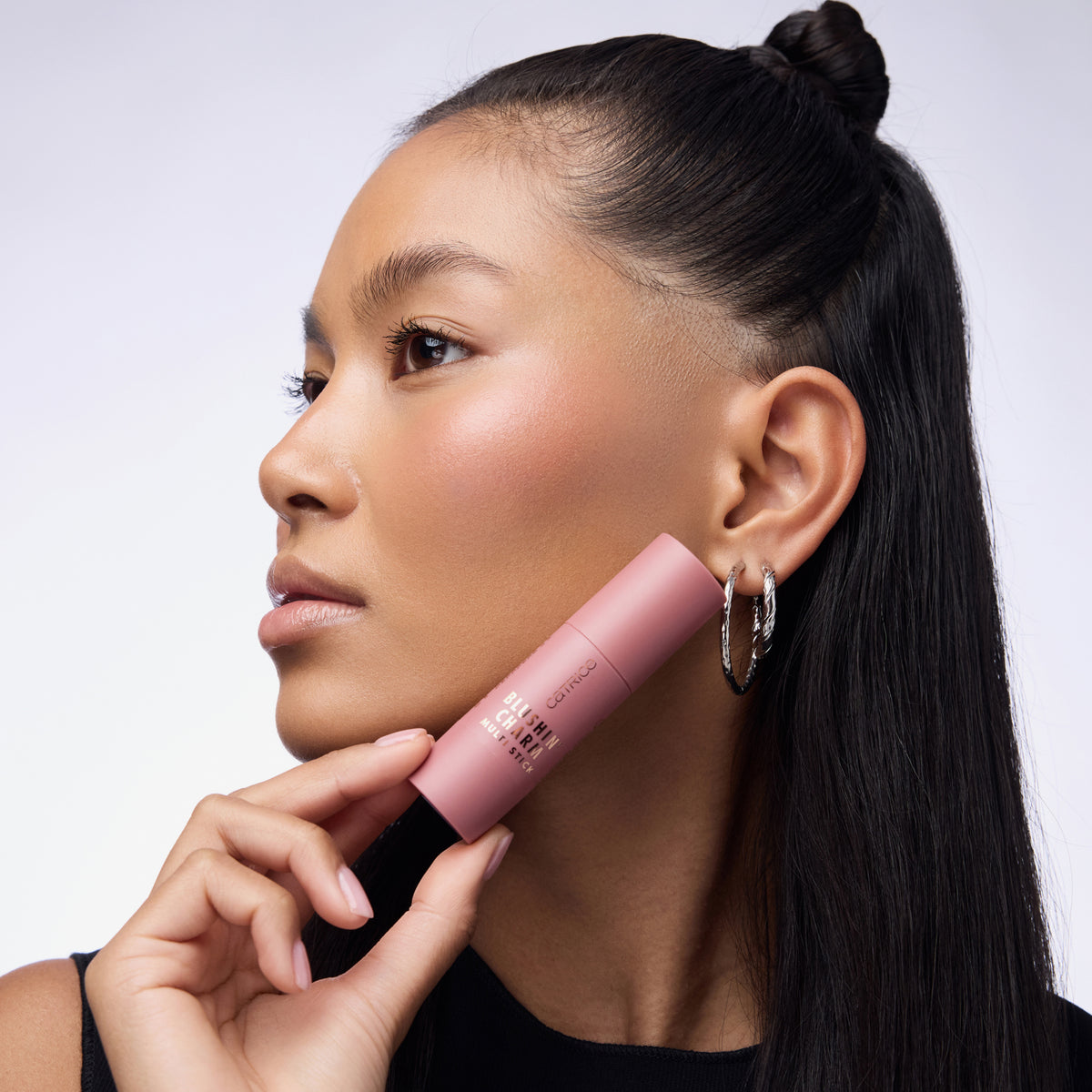 Nahaufnahme einer Frau die den Blushin' Charm Multi Stick 050 auf den Wangen trägt und den Stick an ihr Gesicht hält..