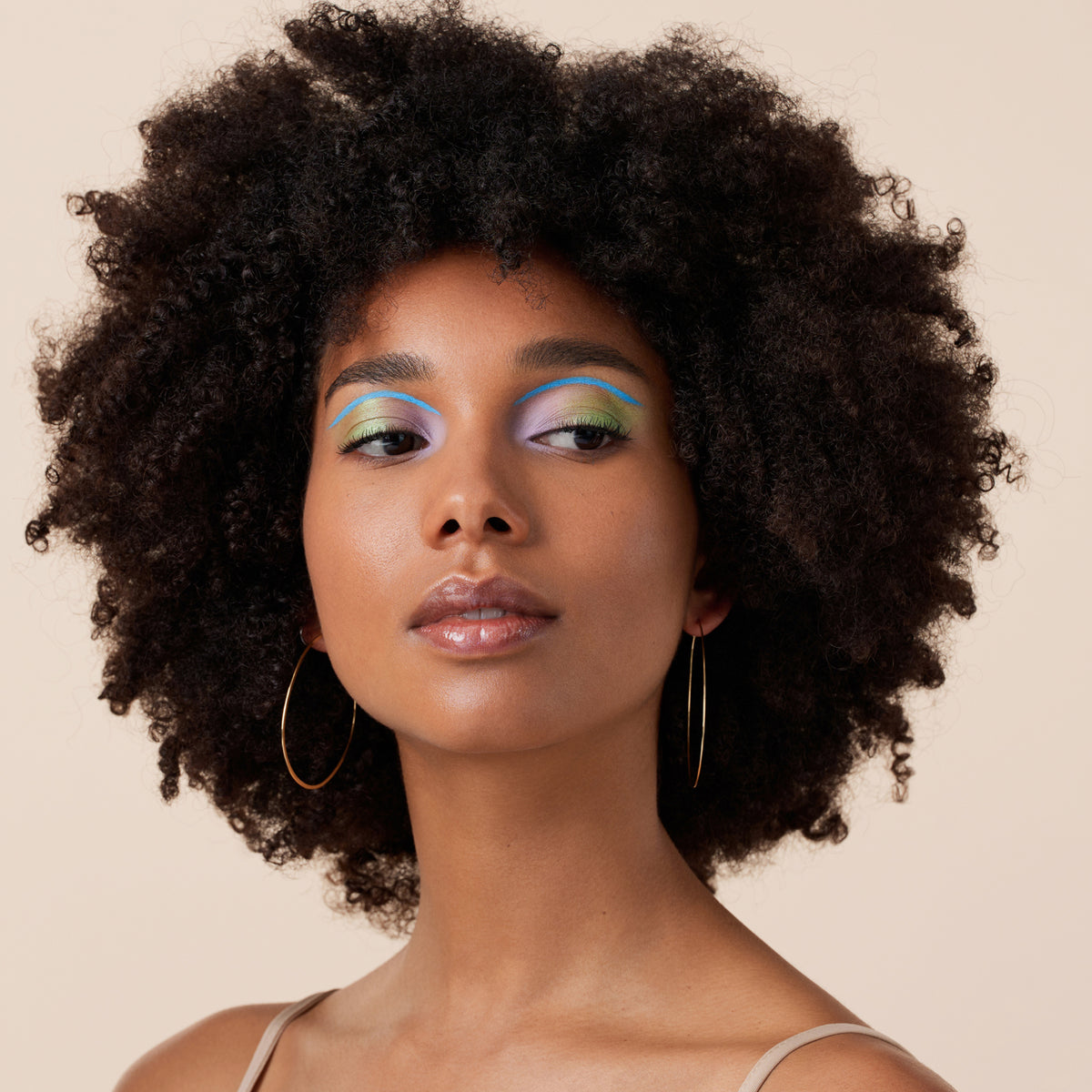 Eine Frau mit Afro und buntem Augen-Make-up rundet ihren Look mit dem Melted Sun Cream Bronzer ab.