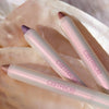 Drei PEARLFECTION Eyeshadow Sticks von Catrice in Rosa, Lila und Roségold sind auf einer strukturierten Oberfläche angeordnet.