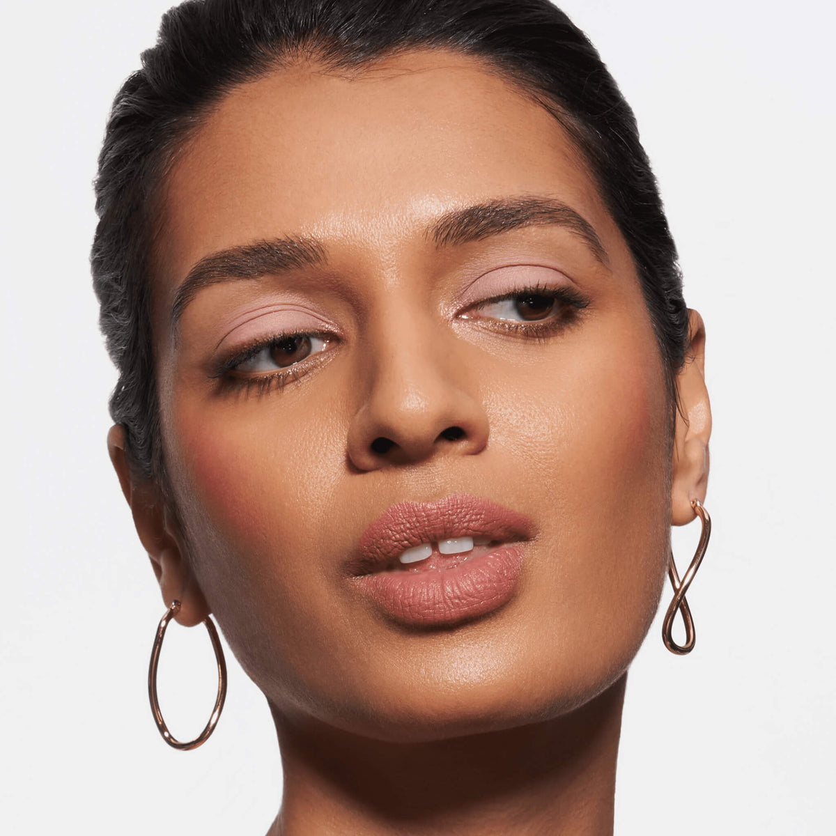 Eine Frau mit natürlichem Make-up, aufgewertet durch den Slim’Matic Ultra Precise Brow Pencil Waterproof, blickt vor einem weißen Hintergrund zur Seite.