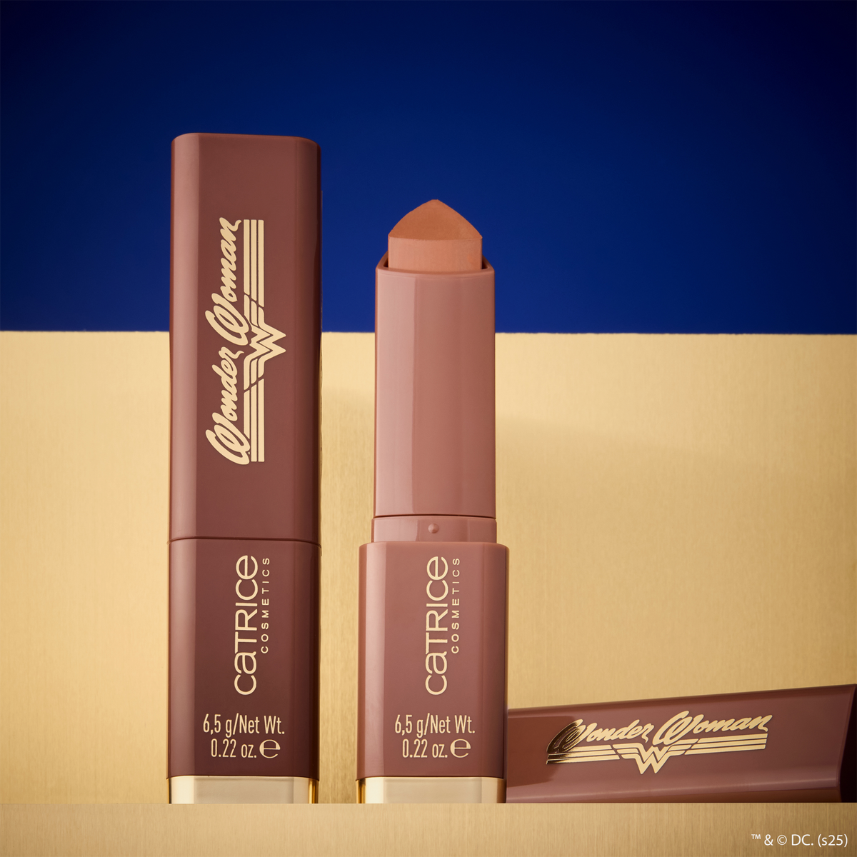 Catrice Wonder Woman Butter Bronzer Stick mit einem goldenen Logo auf einem gold-blauen Hintergrund.