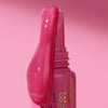 Nahaufnahme des KISS & GLOW Peptide Lip Tint C01 Applikators, aus dem der Gloss heruntertropft, vor einem rosa Hintergrund.