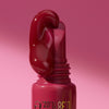 Nahaufnahme des KISS & GLOW Peptide Lip Tint C03 in Rot, wobei der Gloss aus dem Applikator herunterfließt; vor pinkem Hintergrund.