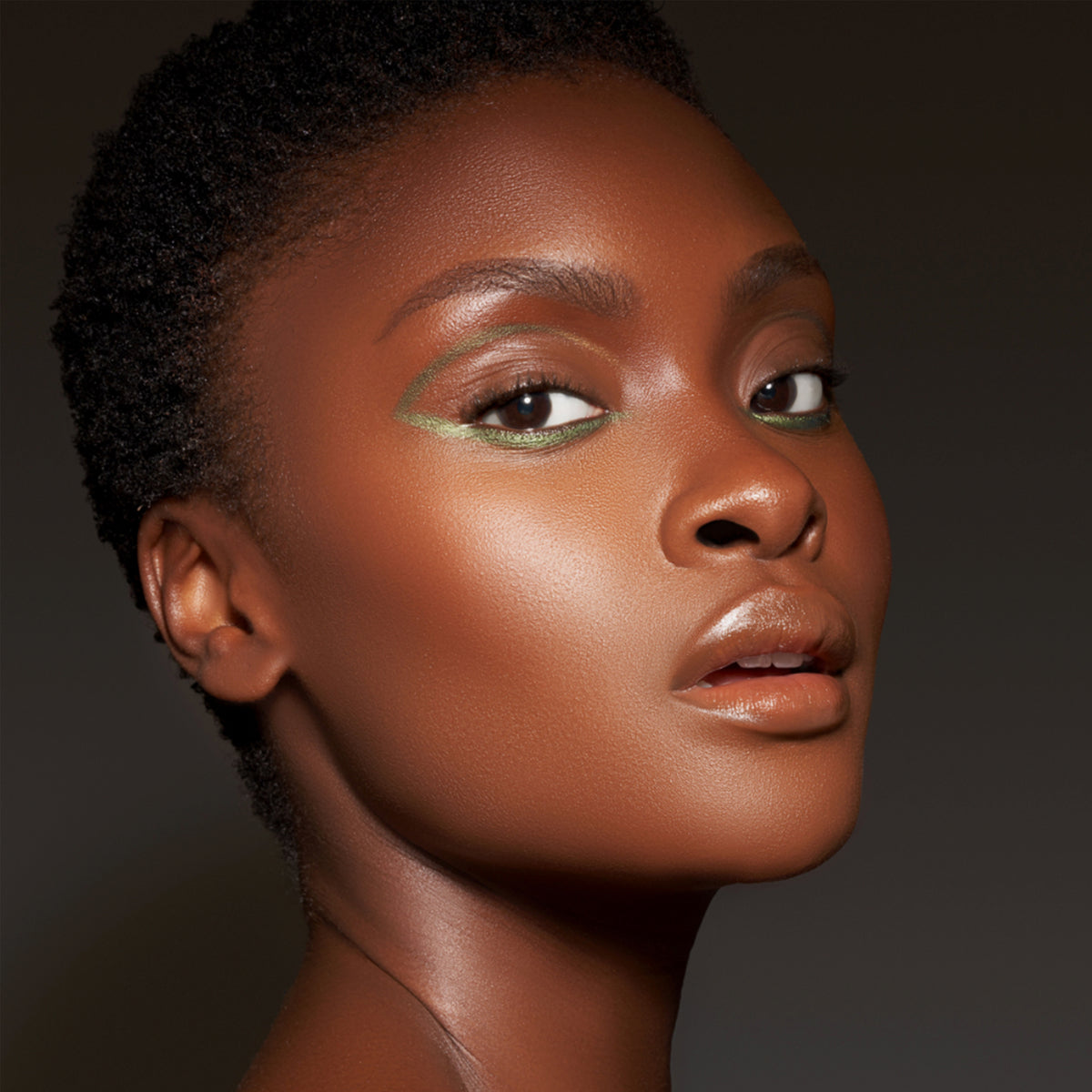 Eine Frau mit dunklem Teint präsentiert Make-up-Look mit grünem Infinite Chrome Pencil.