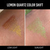 Eine Hand zeigt Farbmuster des Infinite Chrome Pencil Lemon Quartz bei schwachem Licht (orange-gelb schimmernd) und im Sonnenlicht (gelb-grün schimmernd).