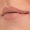 Nahaufnahme der Lippen mit Cream Matte Liquid Lipstick in einem Nude-Ton, an einer Ecke leicht nach oben gezogen, was ein subtiles Grinsen erzeugt.