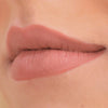 Nahaufnahme der Lippen einer Person, die leicht zur Seite geschürzt ist und einen Cream Matte Liquid Lipstick in einem Nude-Ton trägt.