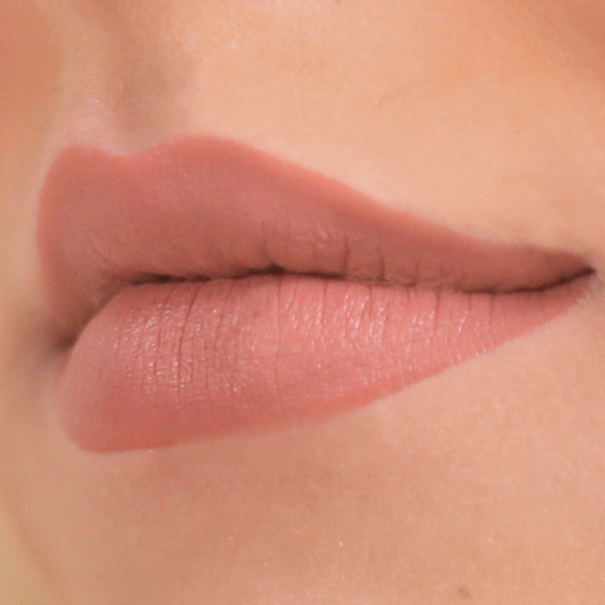 Nahaufnahme der Lippen einer Person, die leicht zur Seite geschürzt ist und einen Cream Matte Liquid Lipstick in einem Nude-Ton trägt.