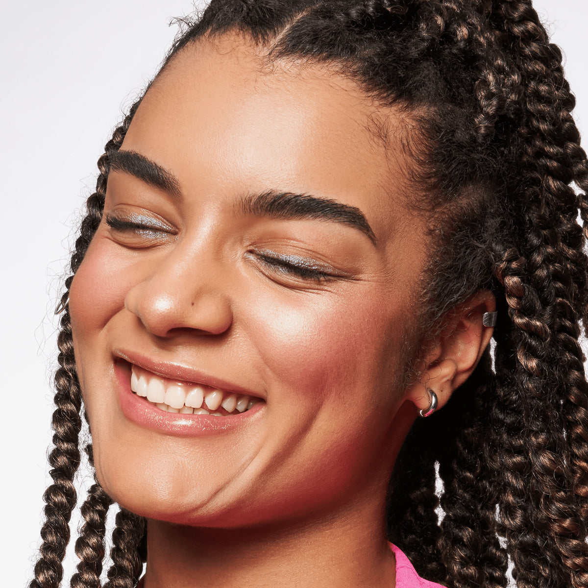 Person mit mittlerem Teint und dunklen Haaren lächelt und präsentiert den BABY GOT GLOW liquid highlighter 30 auf den Wangen.