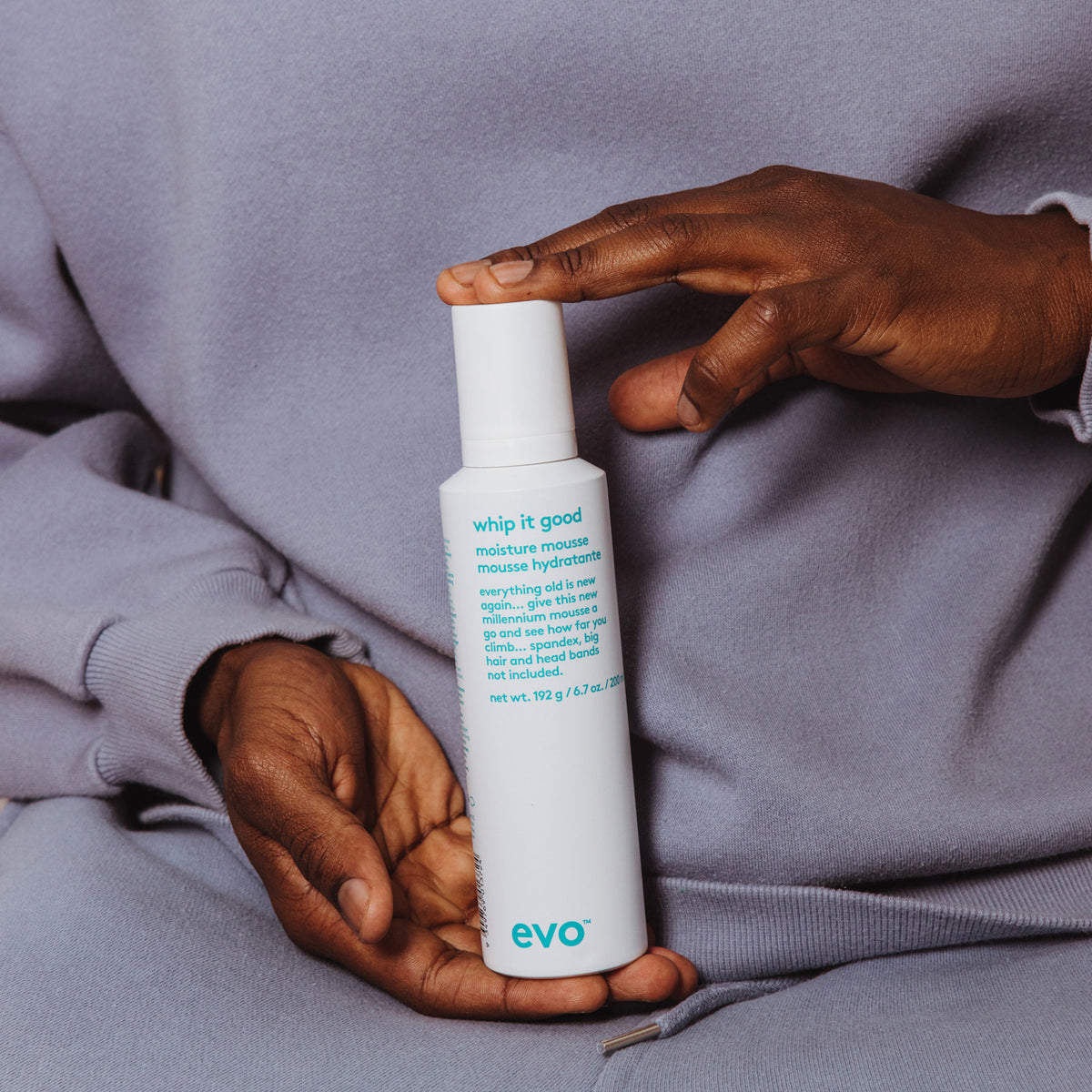 Eine Person in grauer Kleidung hält eine weiße Flasche Whip It Good Moisture Mousse.