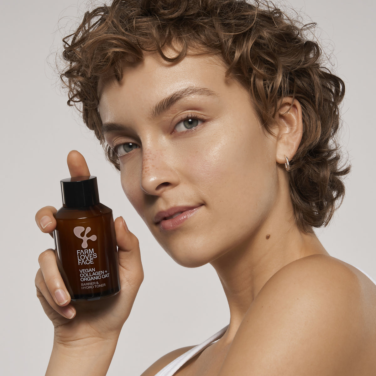 Eine Person hält eine Flasche Vegan Collagen + Organic Oat Barrier & Hydro Toner nah an ihr Gesicht und lächelt leicht.