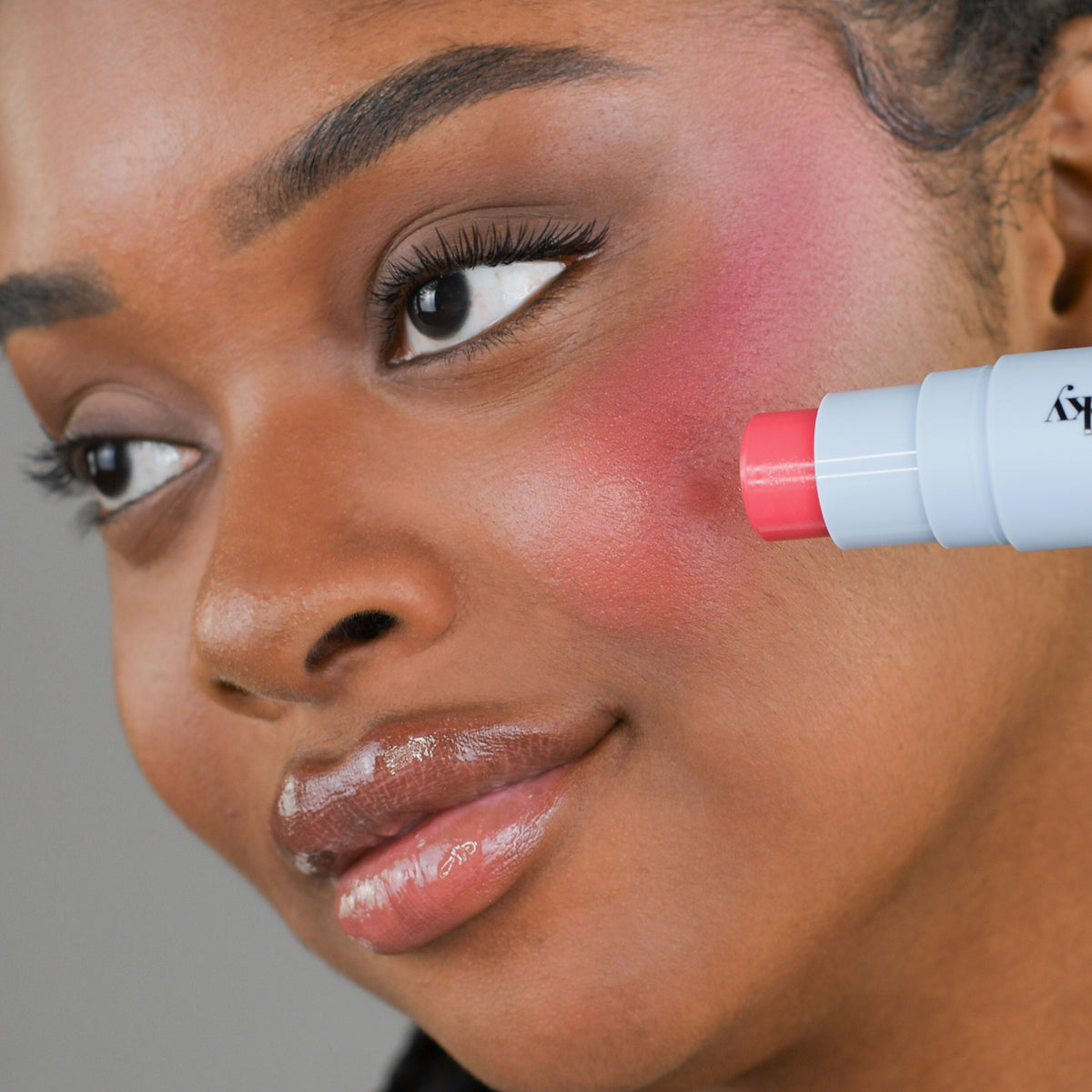 Eine Frau trägt den Blush Stick – 2-in-1 Creme Rouge mit Pinsel Candy auf ihre Wange auf.