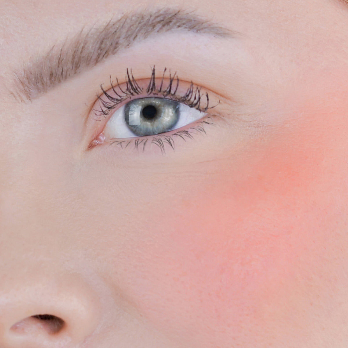 Nahaufnahme des Gesichts einer Person mit rosa Wangen geschminkt mit dem Blush Stick – 2-in-1 Creme Rouge mit Pinsel.