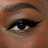 Nahaufnahme eines braunen Auges mit Infinity Ink von LH Cosmetics, das einen kräftigen schwarzen Eyeliner mit Flügeln und lange Wimpern zeigt.