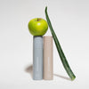 Zwei Flaschen „On set – Subtle glow setting spray“ von LH Cosmetics werden mit einem grünen Apfel und einem Aloe-Vera-Blatt vor einem weißen Hintergrund präsentiert.