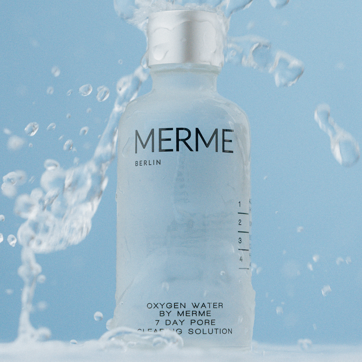 Glasflasche des MERME Oxygen Water 4-Wochen-Sets mit silbernem Deckel mit plätscherndem Wasser vor hellblauem Hintergrund.