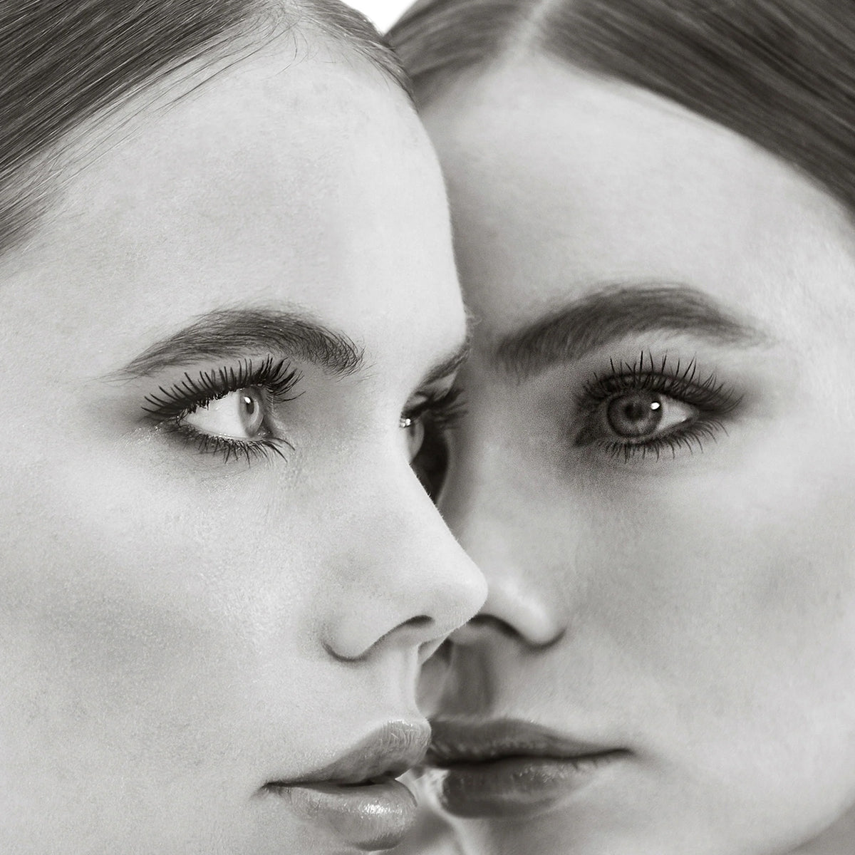 In einem Schwarz-Weiß-Porträt stehen sich zwei Frauen mit ähnlichen Gesichtszügen gegenüber und zeigen die Mascara Femuline™ by Mesauda Beauty.