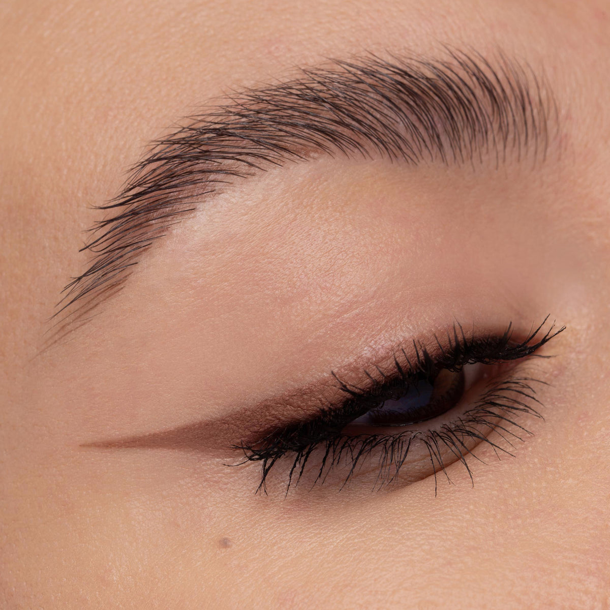 Nahaufnahme eines geschminkten Auges mit einem soften, braunen Wing-Look. Die Linie ist dezent verblendet und betont die natürliche Augenform.