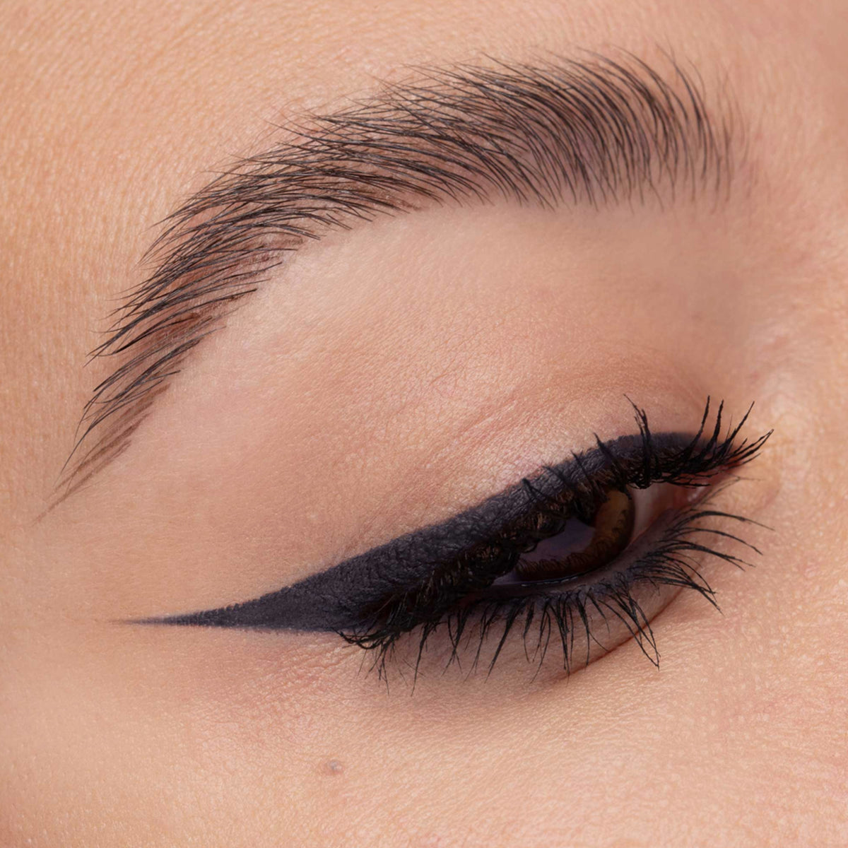 Nahaufnahme eines Auges mit anthrazitfarbenem Eyeliner. Der präzise Wing zieht sich scharf nach außen, Wimpern sind betont.