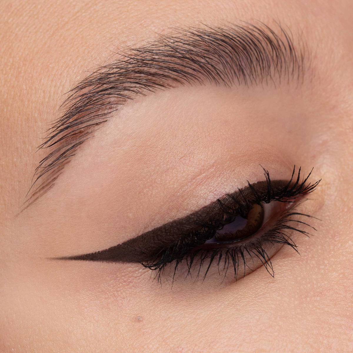 Nahaufnahme eines Auges mit präzisem, dunkelbraunem Eyeliner in Cat-Eye-Form. Der Lidstrich ist scharf gezogen und betont den äußeren Augenwinkel.