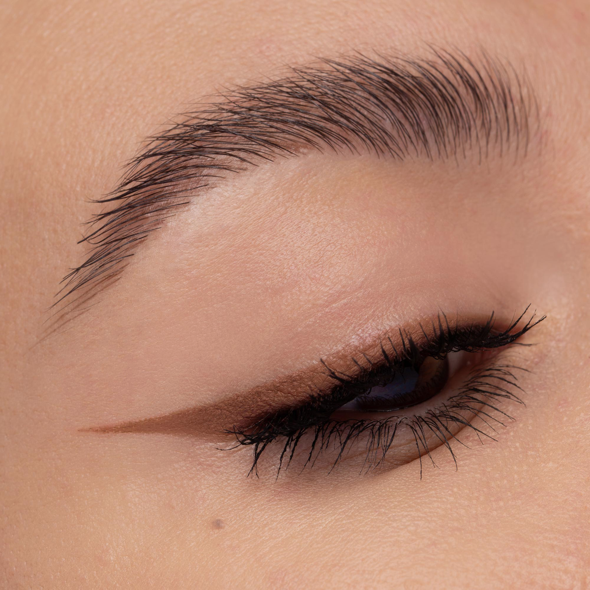 Nahaufnahme eines geschminkten Auges mit braunem Lidschatten und präzisem, mattem braunen Eyeliner-Wing. Wimpern sind leicht getuscht.