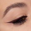 Nahaufnahme eines Auges mit beerenfarbigem Eyeliner. Der präzise Wing zieht sich scharf nach außen, Wimpern sind betont.