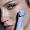 Eine Frau hält Vicious Mascara Waterproof mit einer katzenförmigen Kappe vor ihr Gesicht und betont so ihre langen Wimpern.