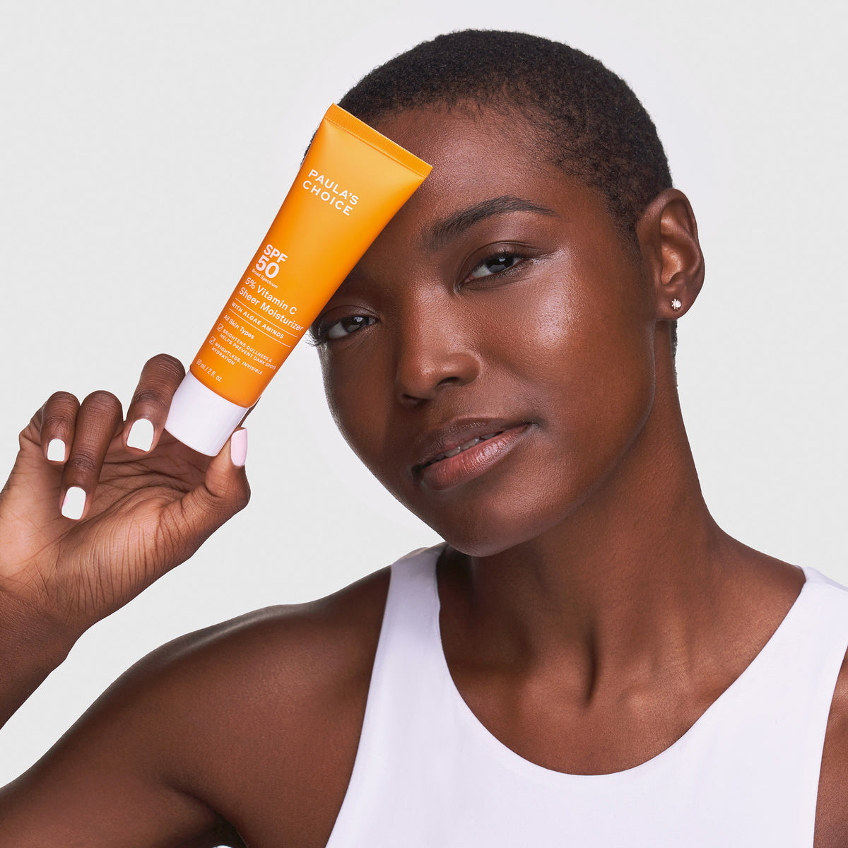 Eine Person hält eine Tube Paula’s Choice 5 % Vitamin C Sheer Tagescreme LSF 50 SPF vor ihr Gesicht.