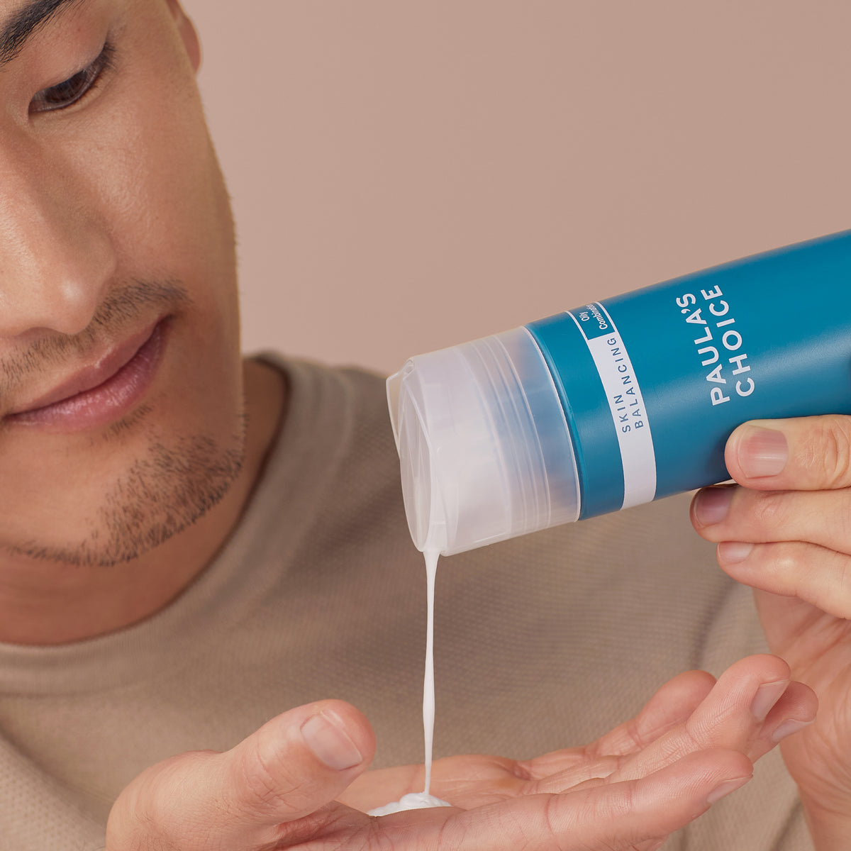 Eine Person gießt Skin Balancing Oil-Reducing Cleanser aus einer blauen Flasche in ihre Handfläche.