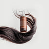 Das Hair Density Scalp Treatment in einer braunen Pumpflasche ist umgeben von wallenden dunklen Haarsträhnen vor hellem Hintergrund.