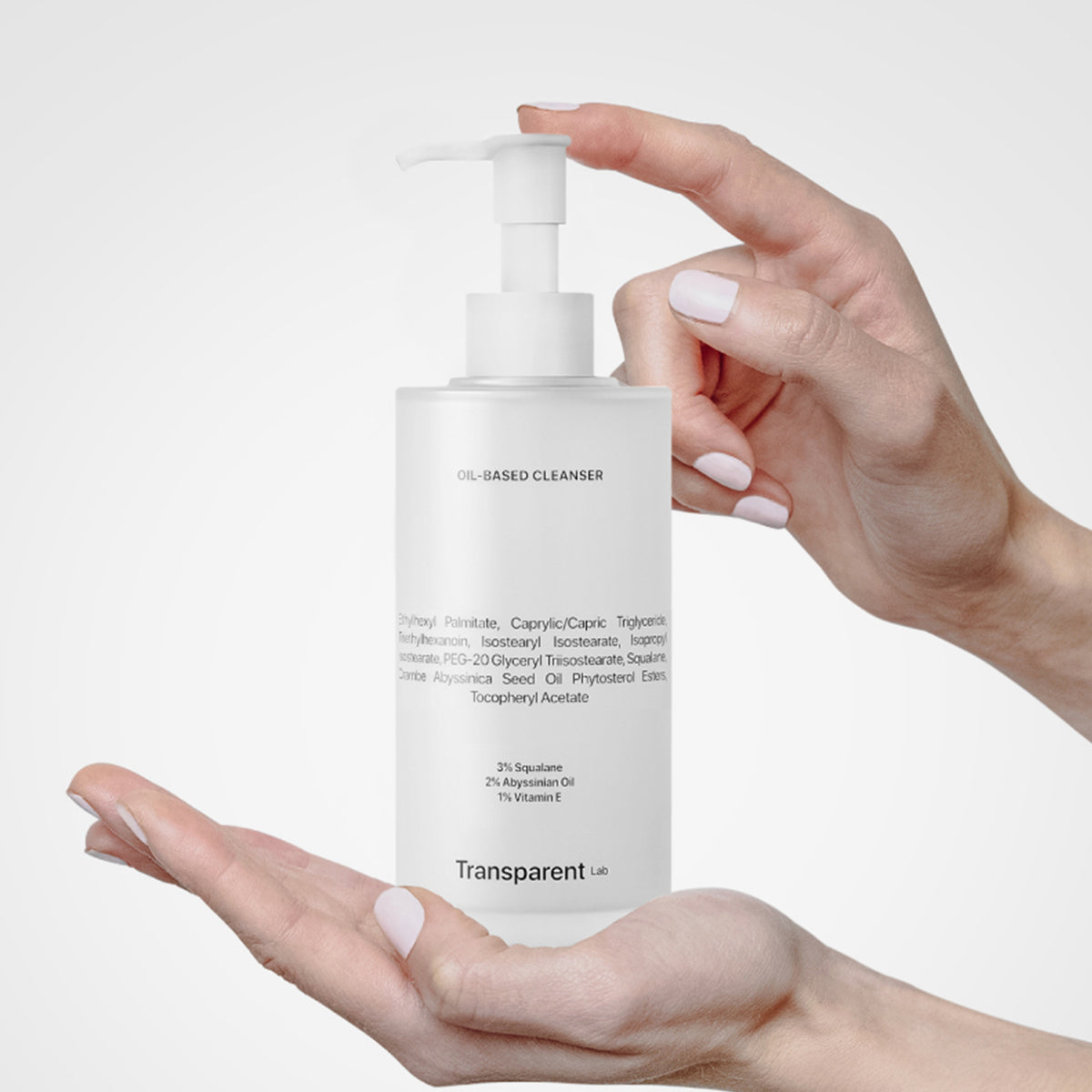 Jemand hält vor einem hellen Hintergrund eine Pumpflasche mit ölbasiertem Reiniger von Transparent Lab in der Hand.