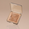 Skin Bronzing kompaktes, strukturiertes Puder-Make-up mit NABLA-Prägung in einer durchsichtigen, quadratischen Hülle auf beigem Hintergrund.