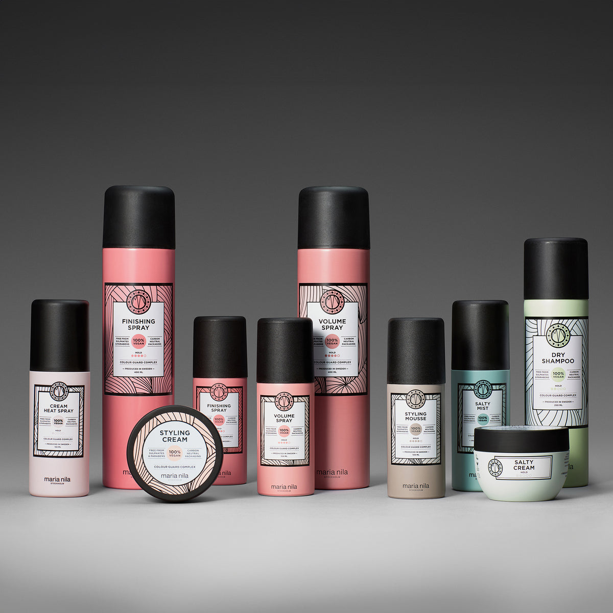 Mehrere farbige Haarstyling-Produkte von Maria Nila vor grauem Hintergrund.