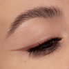 Nahaufnahme des Auges einer Person mit braunem Eyeliner mit Flügeln, der mit Cupid’s Arrow Longwear Stylo gezeichnet wurde, und langen, definierten Wimpern.