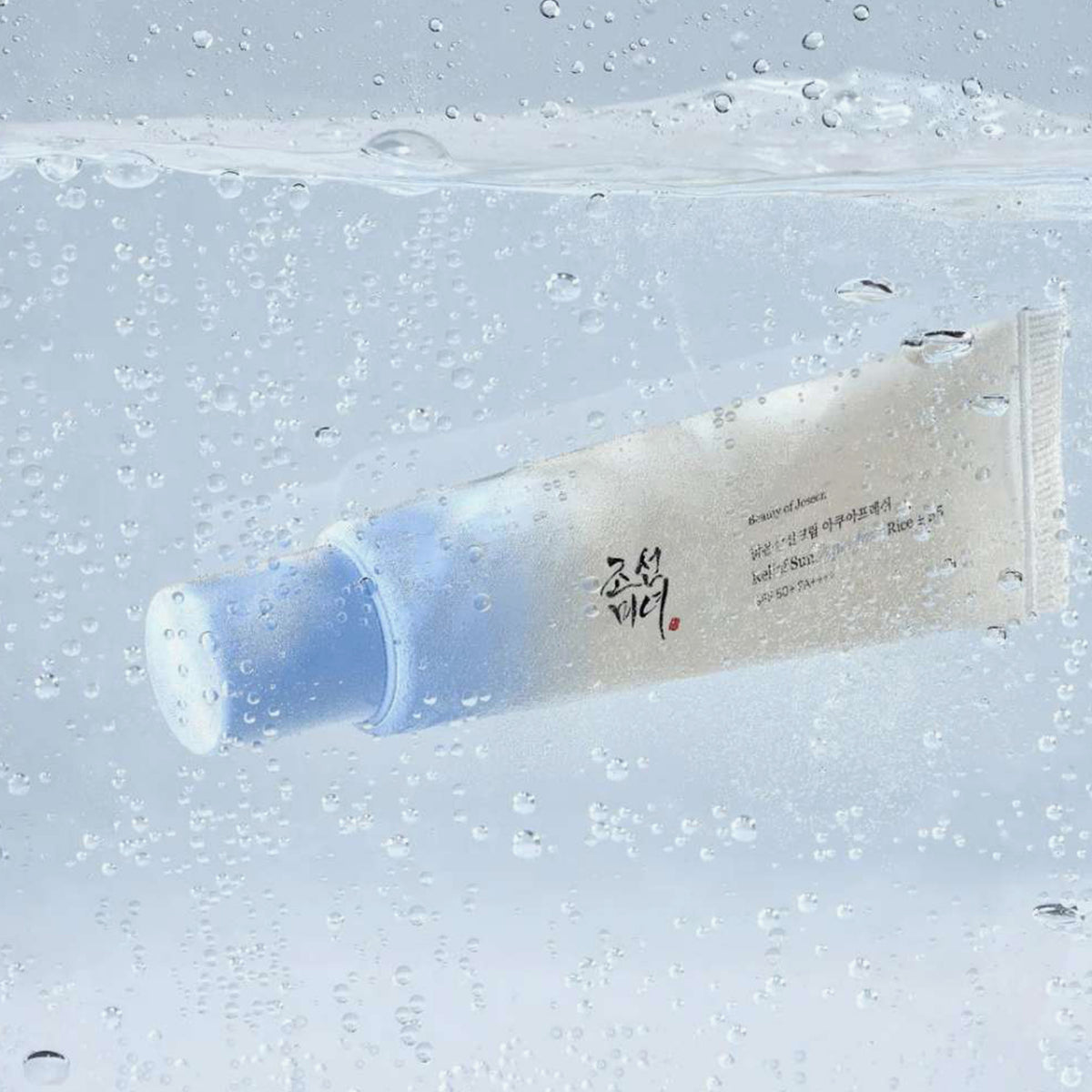 Die Relief Sun Aqua Fresh Rice + B5 SPF 50+ Tube umgeben von Sprudelwasser