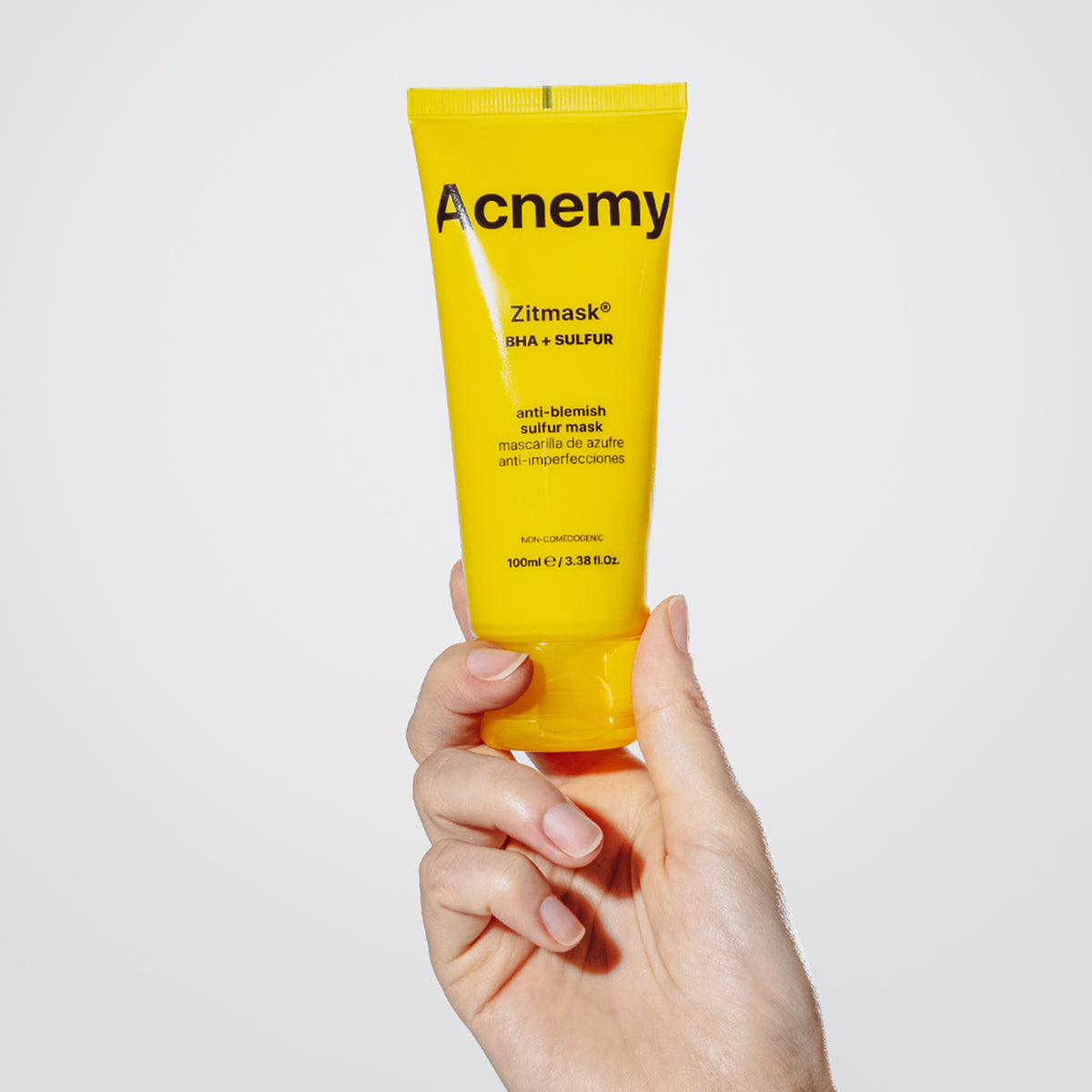 Eine Hand hält eine gelbe Tube Zitmask vor einem schlichten weißen Hintergrund.