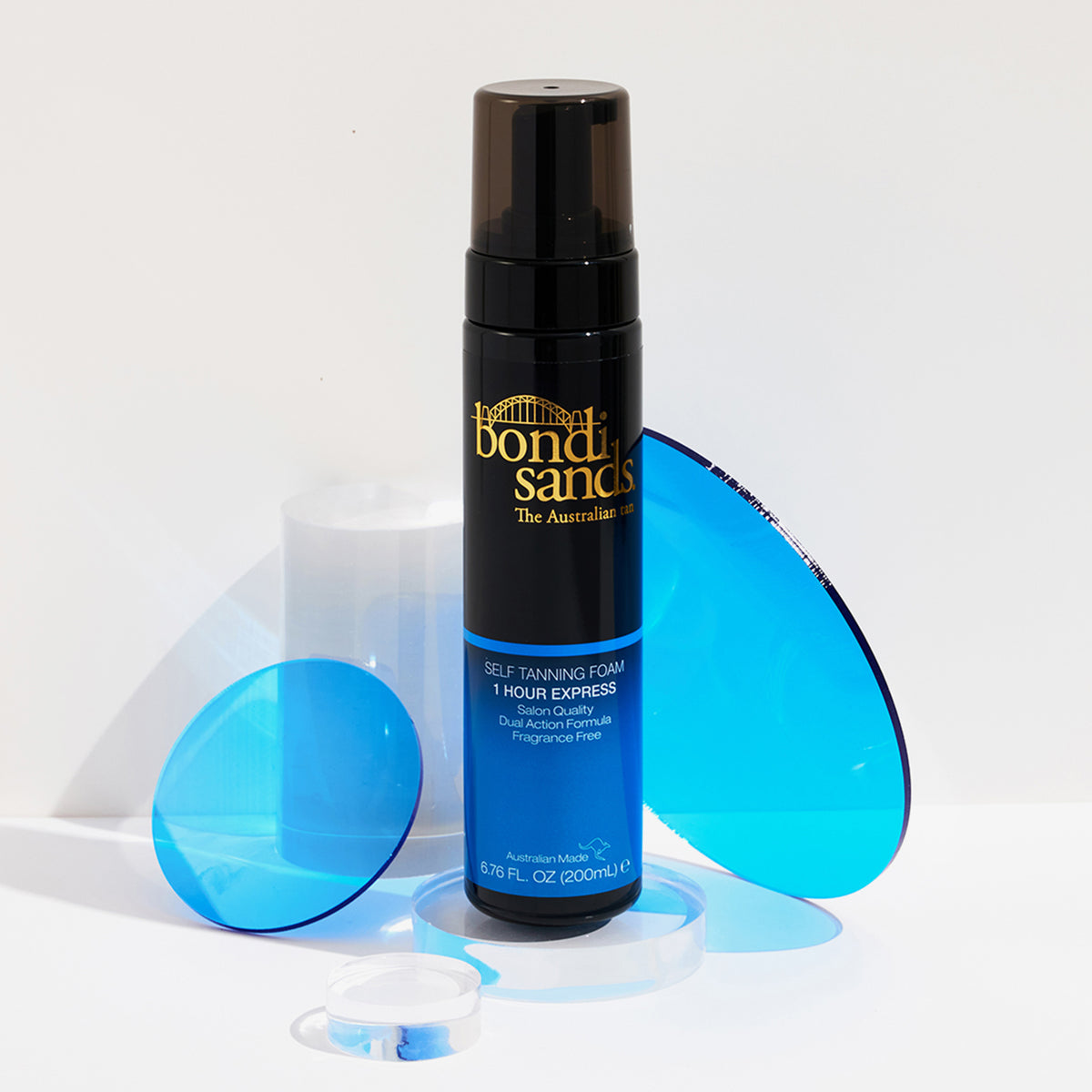 Die Flasche Self Tanning Foam 1 Hour Express von Bondi Sands, präsentiert mit blauen runden Requisiten auf weißem Hintergrund